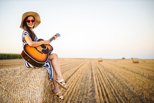 Fashion young woman playing guitar at agriculture field