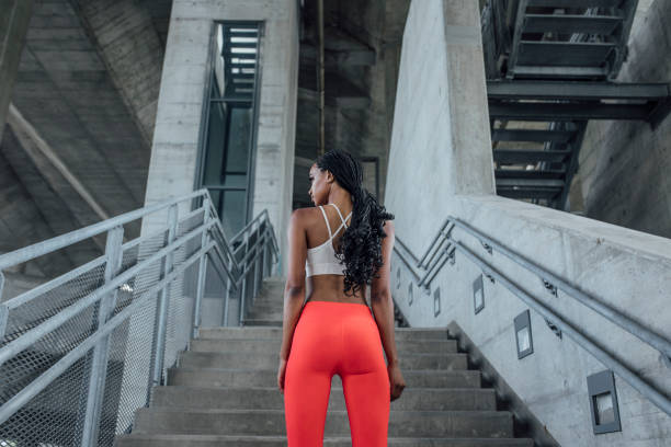 Determined and Ready: Portrait of a Sportswoman in Red Running Tights and Top Standing Outdoors, Back View Ready to work out: back view of African sportswoman standing outdoors. industrial style photos stock pictures, royalty-free photos & images
