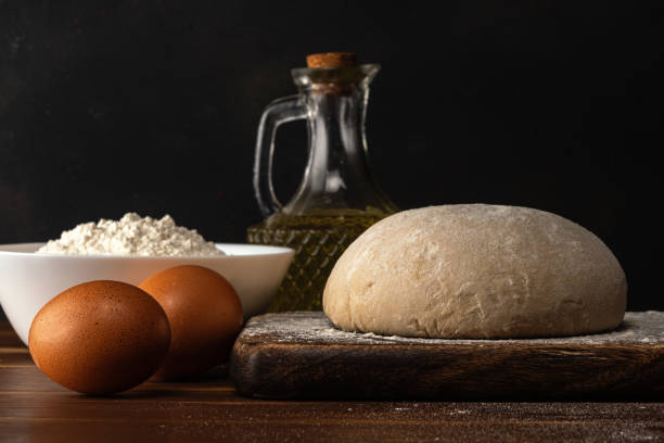 istock Fresh raw dough for bread or pizza with eggs on a dark wooden table. 1221004536