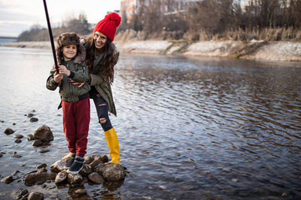 Mother and her little son having fun playing with sticks by the river outdoors in nature.