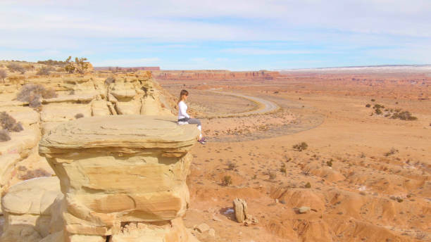 istock aerial: young climber sits on the edge of a rock formation overlooking desert 1221005328