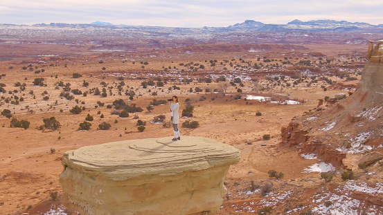 drone: female photographer is taking pictures of the stunning desert in utah. woman stands on top of a boulder and takes photos of the breathtaking canyon in north america. tourist girl photographing.