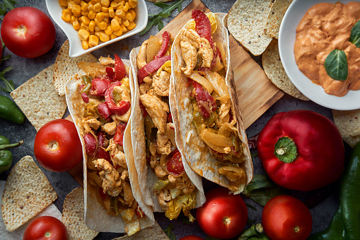 Still life of three fajitas or Mexican tacos with meat, pepper, tomato, spicy pepper and nachos. Mexican food concept.