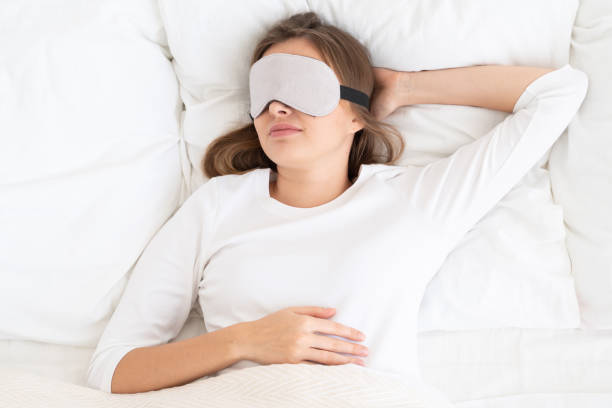 istock Young girl having rest in her bed with white sheets, wearing gray eyemask isolating her from sunlight, sleeping peacefully, relaxing 1221008958