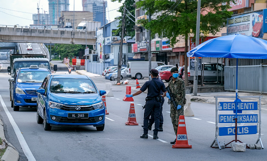 Kuala Lumpur, Malaysia - April 19, 2020: Malaysia soldier and police inspect road users at a roadblock to enforce the order to stay at home, during the Movement Control Order COVID-19 outbreak.