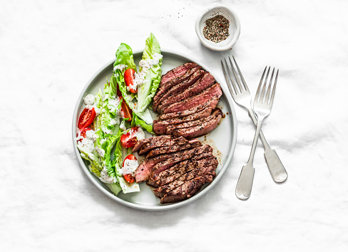 Medium rare beef steak and romaine cherry tomatoes yogurt dressing salad on a light background, top view.Delicious balanced food