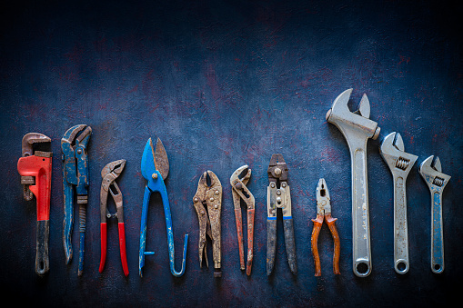 Aged construction hand tools inventory pliers nippers, wrenches, grip, pipe wrench organized in a row on dark gray grunge background