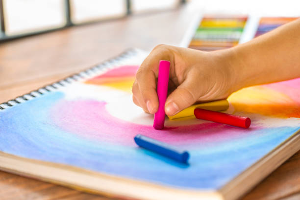 istock girl's hand making a multi-colored drawing with colorful wax crayon 1221021228