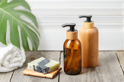 Wooden and glass bathroom accessories without label. Soap bar dish and liquid soap pump dispensers on wooden background