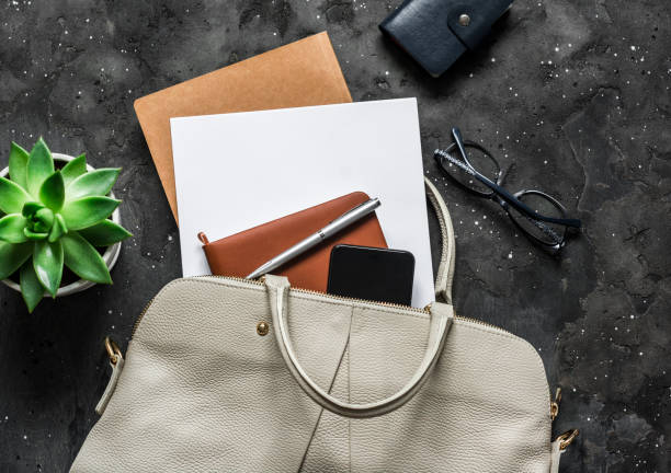 istock Women's white leather bag with office accessories on a dark background, top view. Business concept 1221023209
