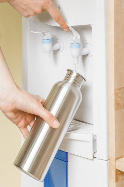 Filling bottle with water from cooler in office Woman pouring water to her personal stainless steel water bottle. Healthy daily habits concept water cooler stock pictures, royalty-free photos & images