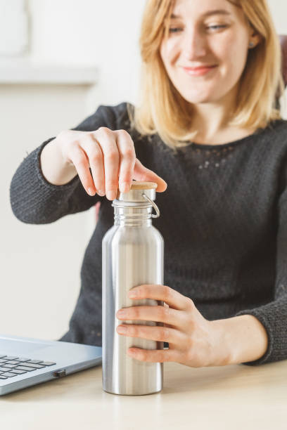 Woman open her metal bottle to drink fresh water Blonde woman opening her metal water bottle to drink fresh water during working day. Healthy daily habits concept bottled water on table stock pictures, royalty-free photos & images