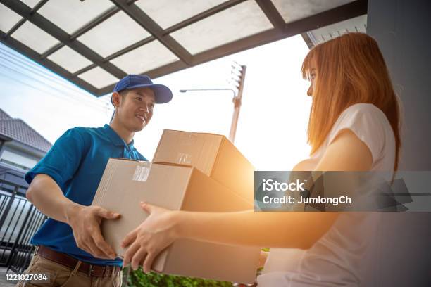 A Young Asian Deliveryman Is Delivering A Package To A Female Customer In Front Of Her House For Her To Sign To Receive The Product After She Ordered The Goods Online During The Outbreak Of The Coronavirus Or Covid19 Virus Stock Photo - Download Image Now