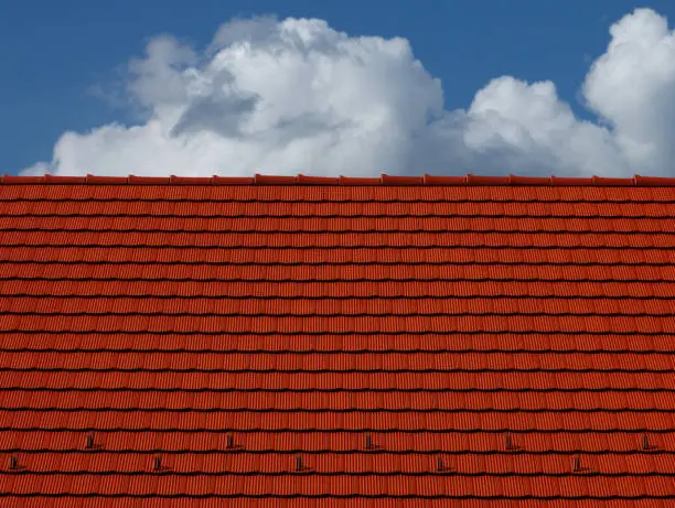 sloped red clay tile roof and ridge. clear blue sky in day light. construction, modern building materials and technology concept. abstract low angle view.