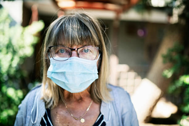 Scared and depressed senior woman during COVID-19 quarantine Portrait of a senior woman wearing anti virus mask in front of her house. The woman seems to be scared and depressed. 
BMPCC4K, RAW Q0 prison lockdown stock pictures, royalty-free photos & images