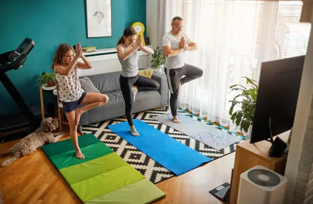 Father and his two daughters practicing yoga with online classes.