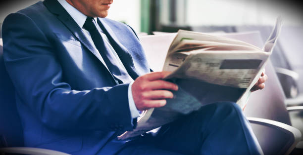 hombre de negocios maduro sentado y leyendo periódico mientras espera para abordar en el aeropuerto - airport newspaper travel business travel fotografías e imágenes de stock