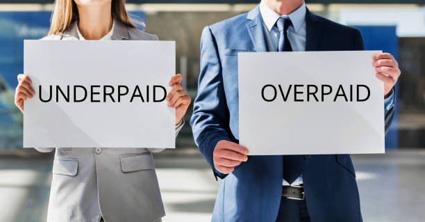 istock Business people holding UNDERPAID and OVERPAID white placard 1221034664