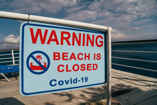 Photo of Beach is closed due to Covid-19 warning sign located at an entrance to a beach. Social media campaign for coronavirus prevention. Summer is cancelled, shutdown concept