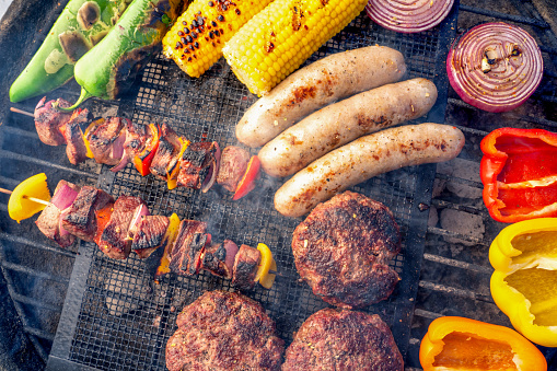 Peppers, Green Chilis, Corn, Onion, Hamburgers, Brats, and Kabobs arranged on a charcoal grill