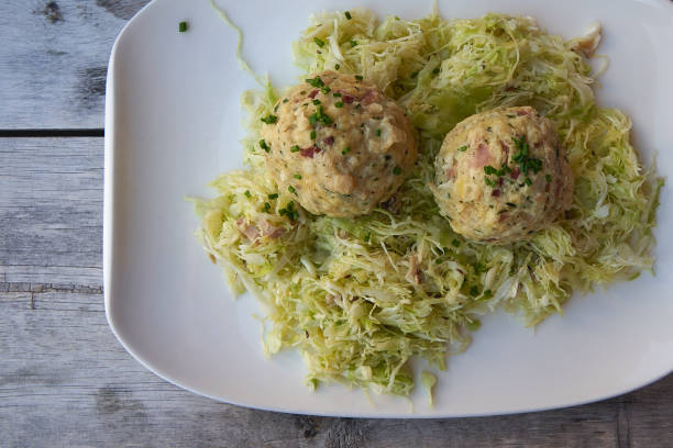 A plate of Tyrolean Canederli (Knödel in German), typical alpine bread dumplings, served with a cabbage and speck salad on a wooden table. Landscape format.