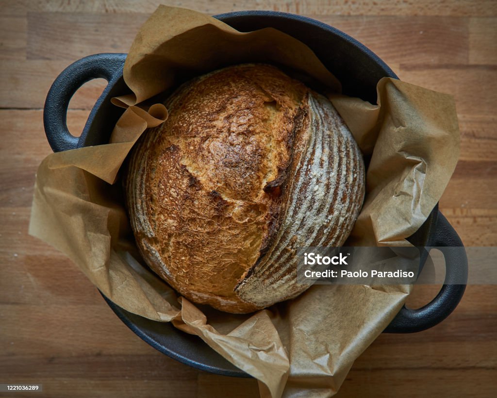 Homemade sourdough bread in a dutch oven on a wooden board. Homemade sourdough bread in a dutch oven on a wooden board. Top view. Landscape format. Sourdough Bread Stock Photo