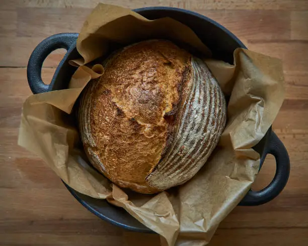 Photo of Homemade sourdough bread in a dutch oven on a wooden board.