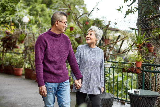 Relaxed Chinese Senior Couple Holding Hands and Walking Front view of Chinese seniors wearing casual clothing and smiling at each other as they hold hands and enjoy outdoor walk. chinese couple stock pictures, royalty-free photos & images