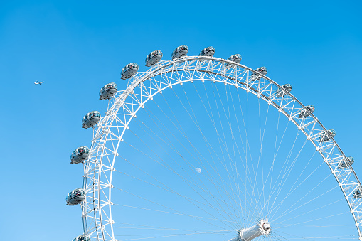 London, UK - June 22, 2018: Closeup view on London Eye wheel on summer day with airplane in blue clear sky and people riding in capsules on Cantilevered structure