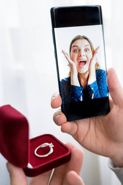 Online video call,marriage proposal to girlfriend by mobile phone, cell.Engagement,wedding.Diamond ring, red box.Man:will you marry me.Surprised,shocked woman says yes.Quarantine,coronavirus,covid-19. videollamada en línea, propuesta de matrimonio a la novia por teléfono móvil, celular. compromiso, boda. anillo de diamantes, caja roja. hombre: te casarás conmigo. una mujer sorprendida, sorprendida dice que sí. cuarentena,coronavirus,cóvido-19