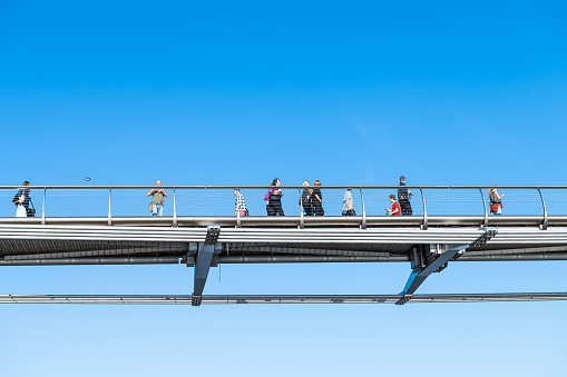 London, UK - June 22, 2018: People walking on city Millennium bridge with pedestrians crossing Thames River closeup isolated against blue sky