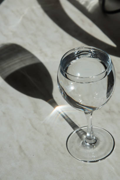 istock A tall glass stands on the table in the sun. The glass forms a shadow, an interesting geometric pattern. There's water in the glass. Vertical orientation 1221042008