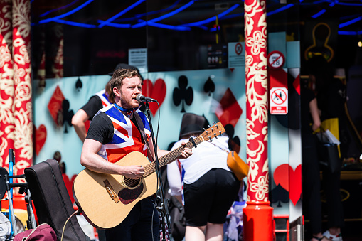 London, UK - June 24, 2018: Piccadilly soho area with patriotic musician playing music on guitar singing in microphone with union jack flag shirt