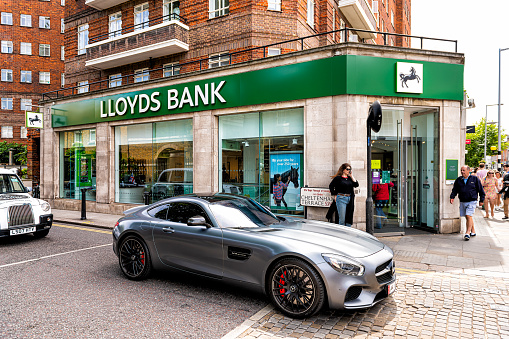 London, UK - June 23, 2018: Green Lloyds Bank sign on branch office building in city with brick architecture and diplomat car in upscale Chelsea neighborhood