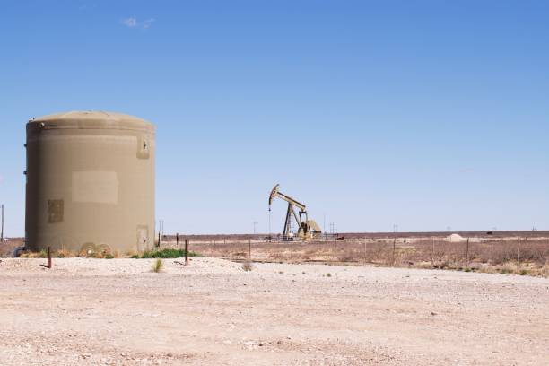 istock Single Pump-jack in distance with water tank in foreground. 1221050404