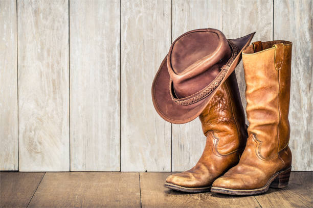 cappello da cowboy retrò wild west e paio di vecchi stivali di pelle su pavimento in legno. foto filtrata in stile vintage - wild west boot shoe cowboy foto e immagini stock