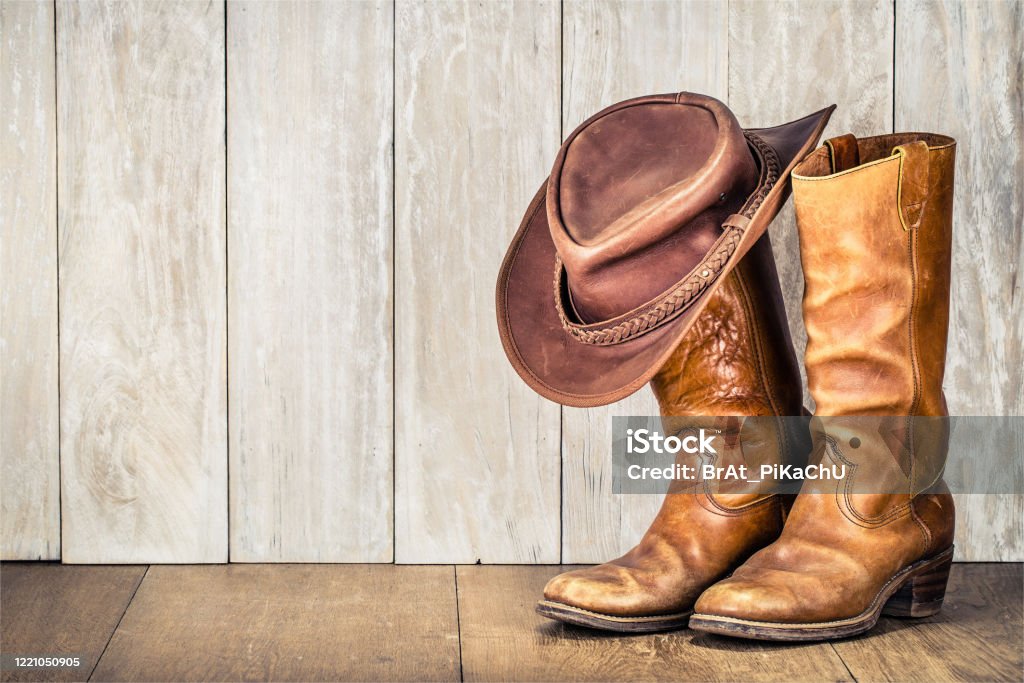 Wild West retro cowboy hat and pair of old leather boots on wooden floor. Vintage style filtered photo Cowboy Hat Stock Photo