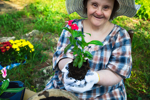 Happy woman with Down Syndrome ready to planting flowers. Activities during Covid-19 in the backyard. Gardening.