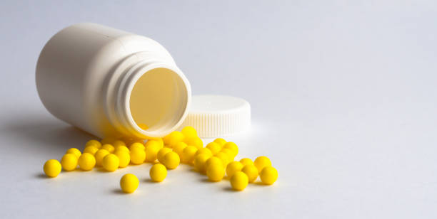 istock Round yellow vitamins are poured out on a white glossy table from a white plastic bottle. Concept. Place for the label. Diagnosis. 1221052186