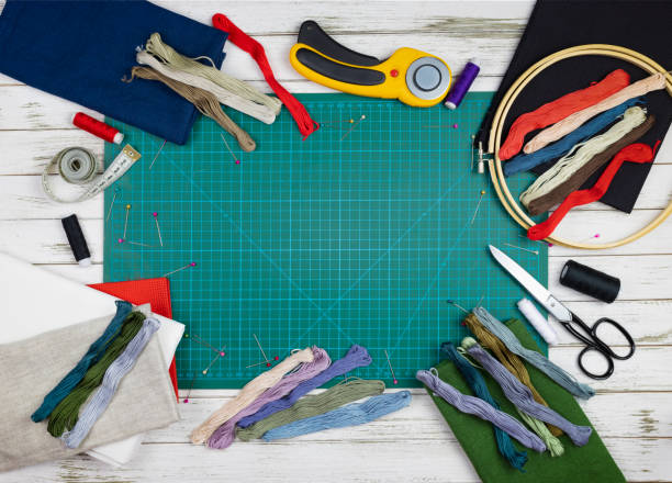 istock quilting, embroidery and sewing tools on the white wooden background. patchwork knife, scissors, lined cutting mat, self-locking, threads, measuring tape, floss, hoop. copy space. flat lay 1221052440