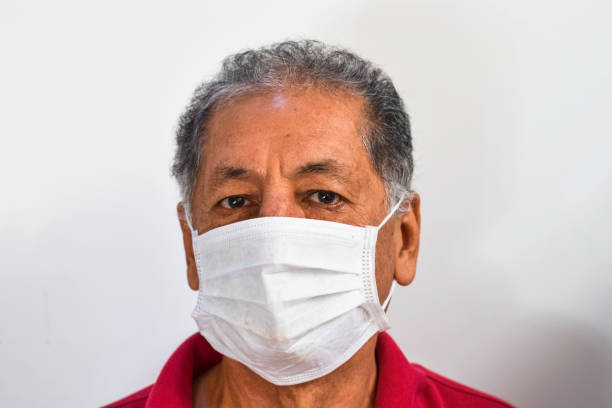 Senior Peruvian man suffers from cough with face mask protection, elderly man with facial mask due to air pollution, sick elderly with medical mask, pollution stock photo