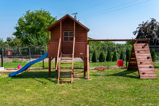 Childrens playground by the house garden, visible wooden house, beautiful spring day.