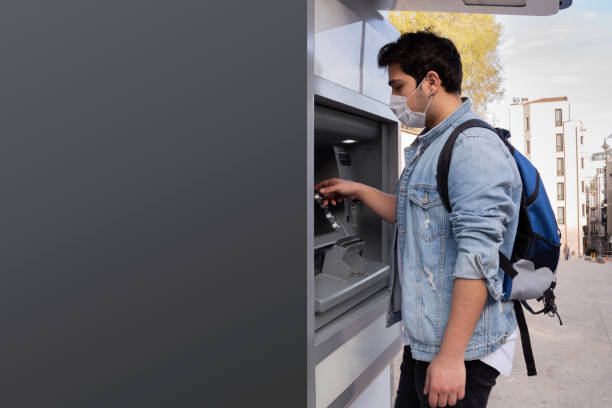 istock The young man performs his transactions from the bank atm using his protective mask. 1221059823
