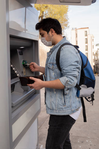 istock The young man performs his transactions from the bank atm using his protective mask. 1221059915