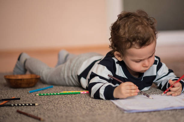 istock Toddler boy lying down on a floor and coloring books with focus 1221060093