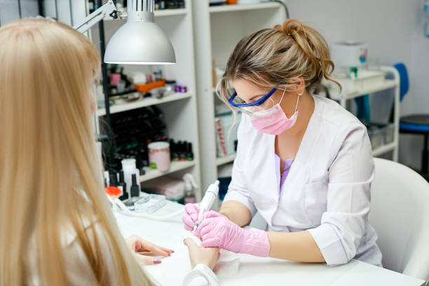 istock Master nail service in goggles and a pink mask performs hardware manicure to the client in the interior of the beauty salon. 1221061292