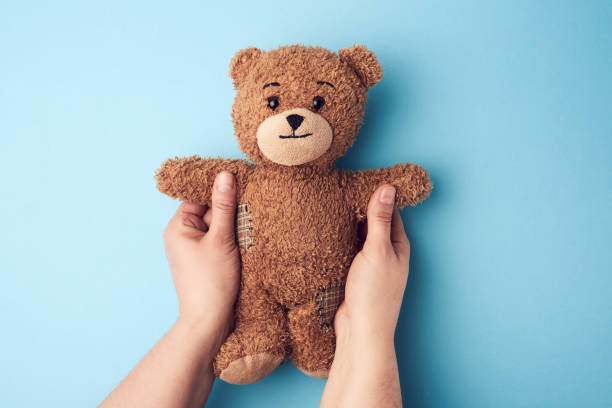 istock two female hands hold a small brown toy teddy bear on a blue bac 1221065814