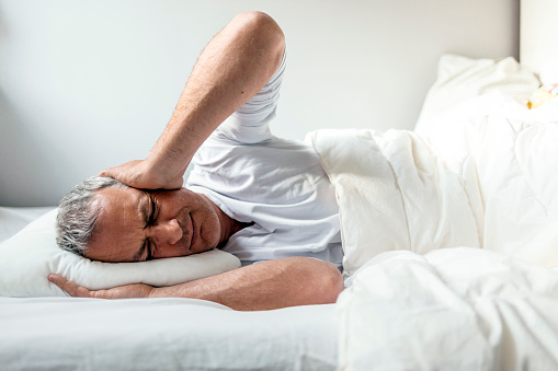 Mature Caucasian man in bed with headache lying in bed during the day.