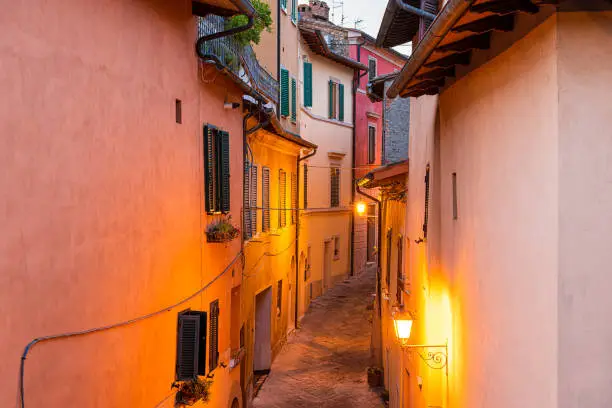 Chiusi, Italy empty street narrow alley in small historic town village in Tuscany during summer evening night with nobody, orange yellow lamp illumination