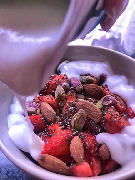 Breakfast or snack bowl composed of oatmeal, fruit with strawberries, nuts with almonds, pistachios and chia seeds, garnishing it with yogurt